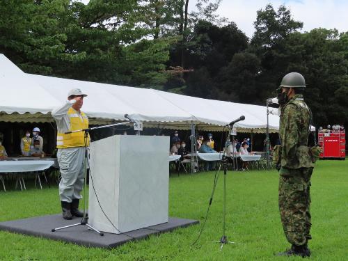 演台で自衛隊員とともに敬礼をする市長の様子