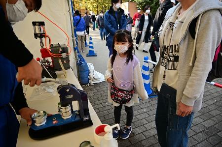 自分で塗ったマンホールの塗り絵が缶バッジになる様子を見守る子の写真