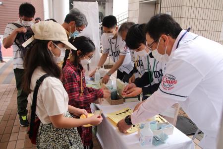 埼玉西武ライオンズのユニフォーム姿で受け付けするボランティアと来場者の女の子ふたり