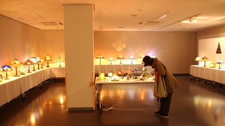  所沢駅東口市民ギャラリーにライトや小物の作品が並んでいる。観覧者が作品を眺めている様子。