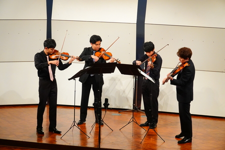 ホールの舞台で4人の演奏者がバイオリンを弾いている