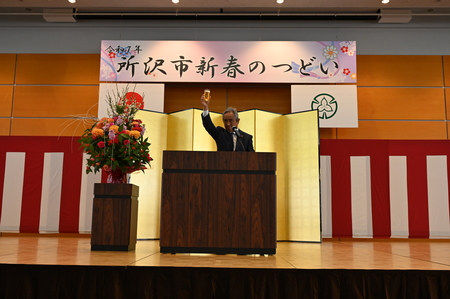 所沢青年会議所の、おぎの会頭がグラスを持ち、ステージ上であいさつしている様子。
