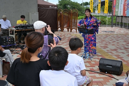 青い浴衣をきて三線を演奏する女性とそれを聞く人々