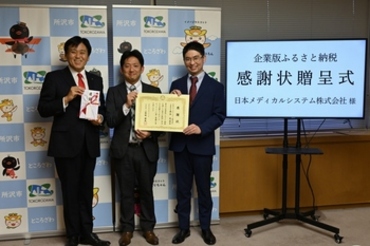 目録を持つ所沢市長と感謝状を持つ日本メディカルシステム株式会社のエリア長統括兼埼玉ゾーン長竹内英介様と薬局長永井直樹様の画像