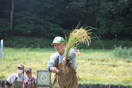 子どもたちの前で稲の刈り方を教えている場面