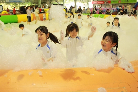 園児たちが泡が入っている巨大ビニールプールで遊んでいる