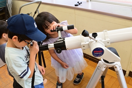 展示されている天体望遠鏡を覗く、こども2人