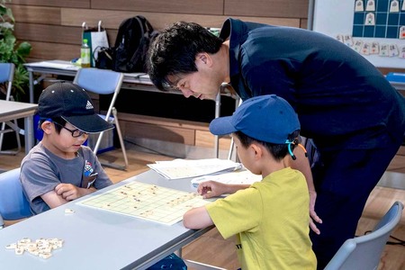 低学年の男の子二人の対局を先生が見ている画像
